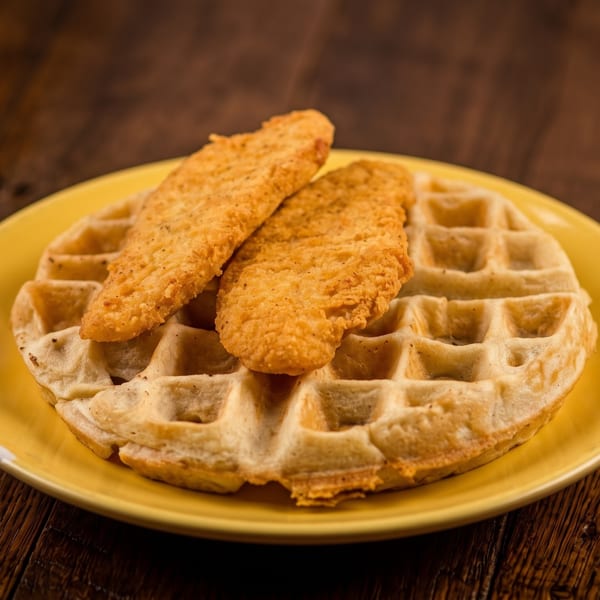 A delicious chicken and waffle dish with two crispy tenders on a yellow plate.