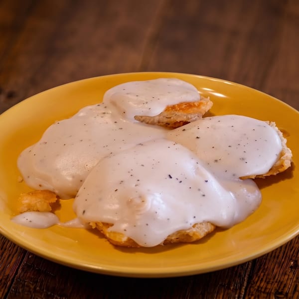 Fluffy biscuits covered in creamy white gravy with black pepper on a yellow plate.