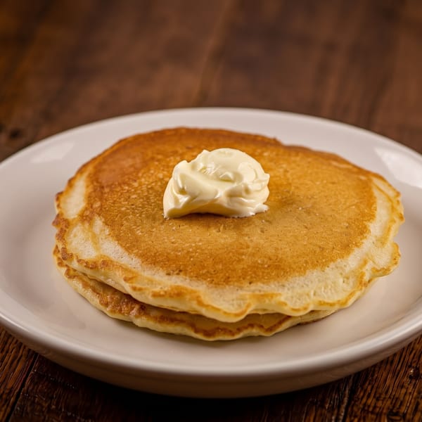 Stack of two golden pancakes with a dollop of butter on a white plate, on a wooden table.