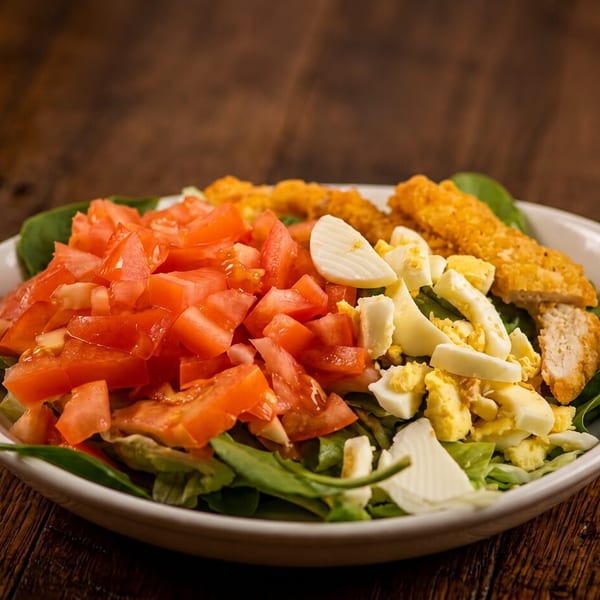 Salad with diced tomatoes, chopped eggs, and crispy chicken strips in a white bowl.
