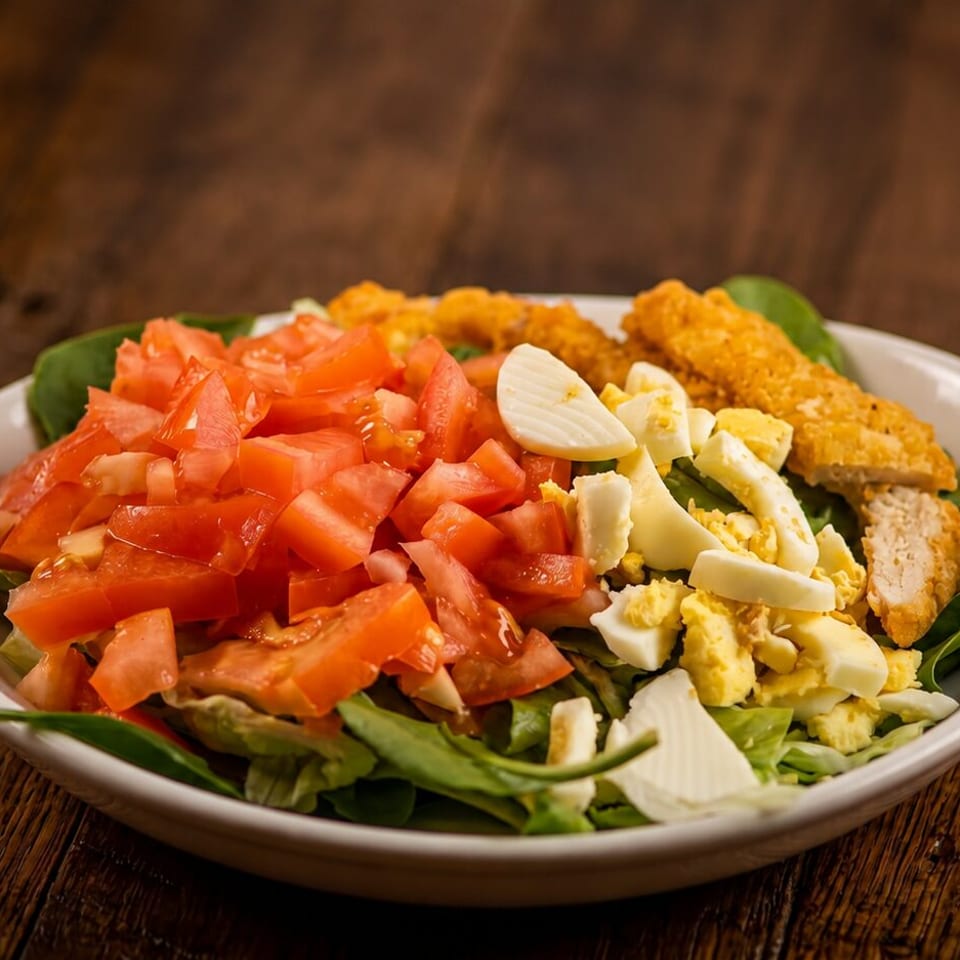 Salad with diced tomatoes, chopped eggs, and crispy chicken strips in a white bowl.